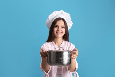 Happy young woman with cooking pot on light blue background