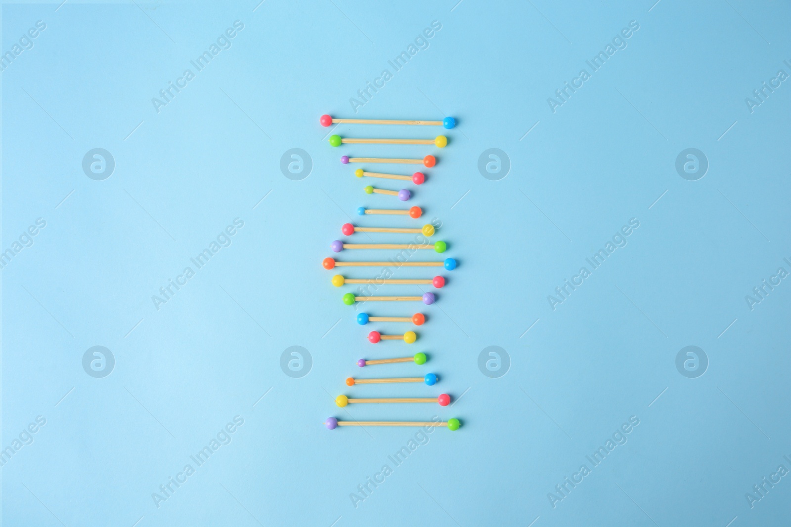 Photo of DNA molecule model made of toothpick and colorful beads on light blue background, flat lay