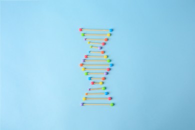 Photo of DNA molecule model made of toothpick and colorful beads on light blue background, flat lay