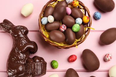 Photo of Chocolate Easter bunny and eggs on pink wooden table, flat lay