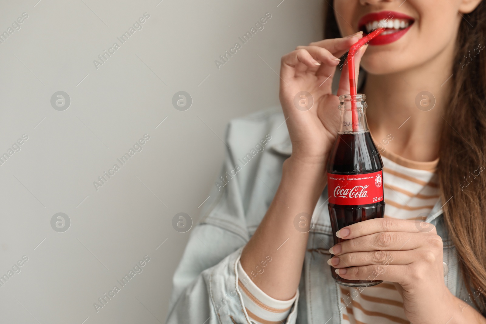 Photo of MYKOLAIV, UKRAINE - NOVEMBER 28, 2018: Young woman with bottle of Coca-Cola on light background, closeup. Space for text