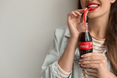 MYKOLAIV, UKRAINE - NOVEMBER 28, 2018: Young woman with bottle of Coca-Cola on light background, closeup. Space for text