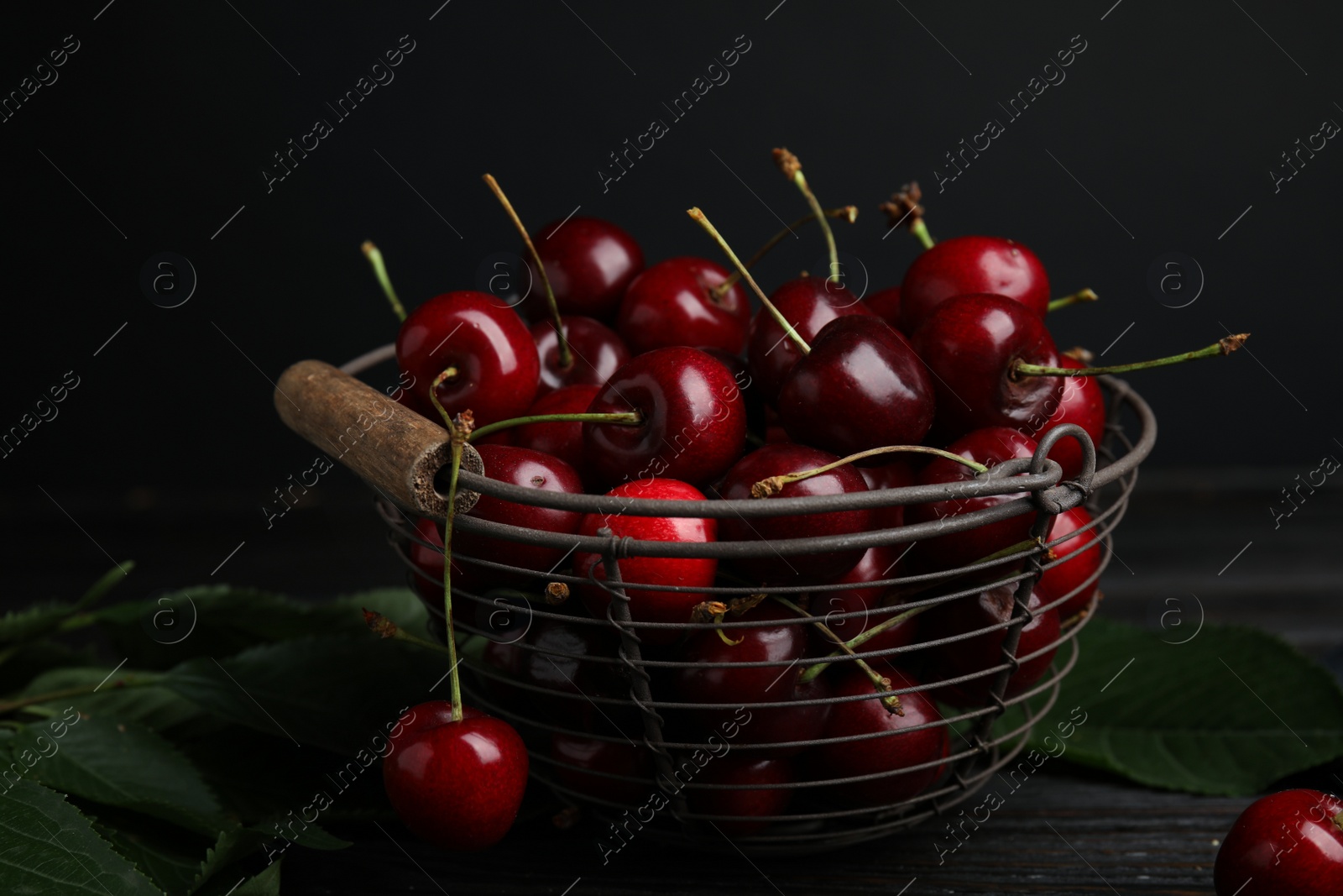 Photo of Metal basket with ripe sweet cherries on dark wooden table