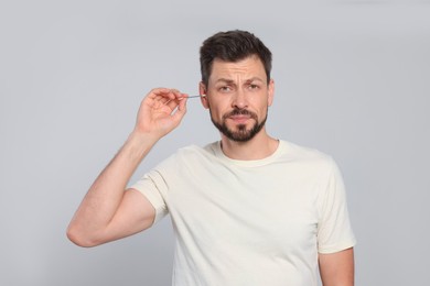 Emotional man cleaning ears on grey background