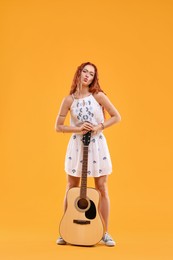 Beautiful young hippie woman with guitar on orange background