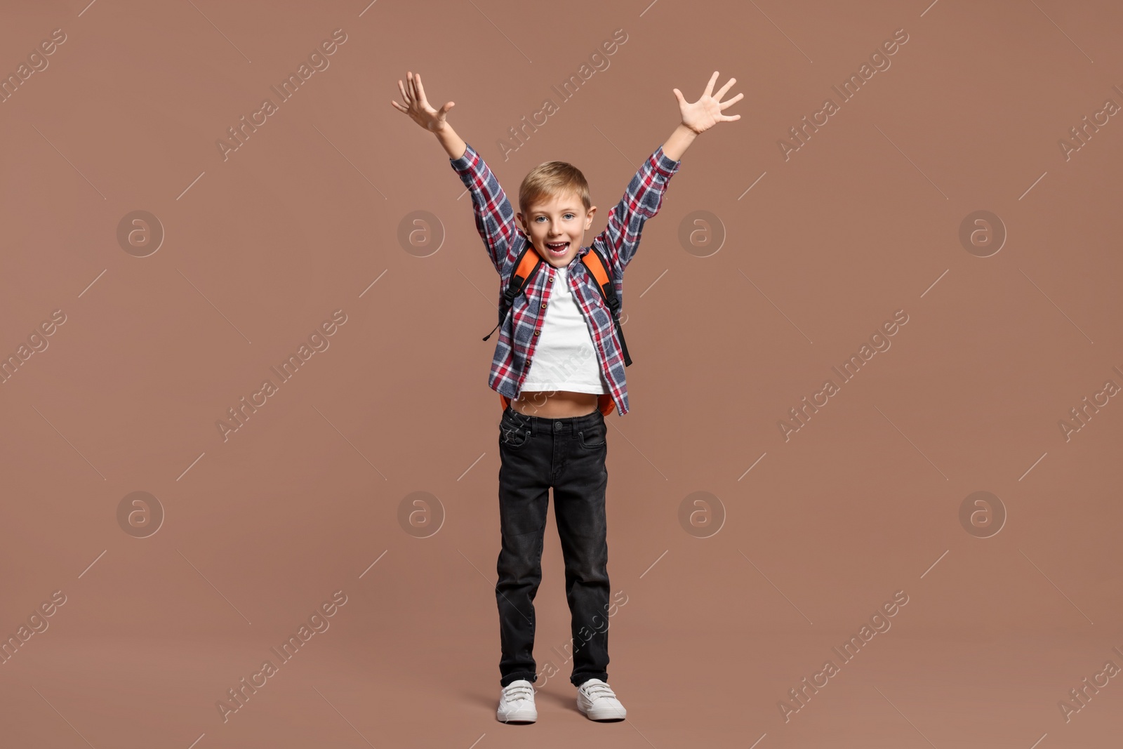 Photo of Emotional schoolboy with backpack on brown background