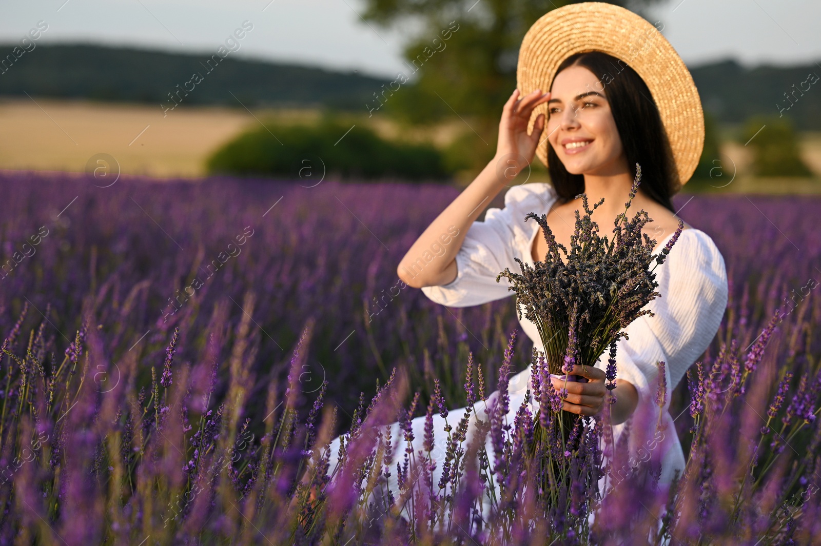 Photo of Beautiful young woman with bouquet sitting in lavender field