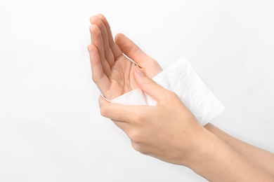 Woman cleaning hands with paper tissue on light background, closeup