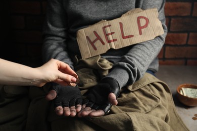 Woman giving coins to poor homeless man with help sign, closeup. Charity and donation