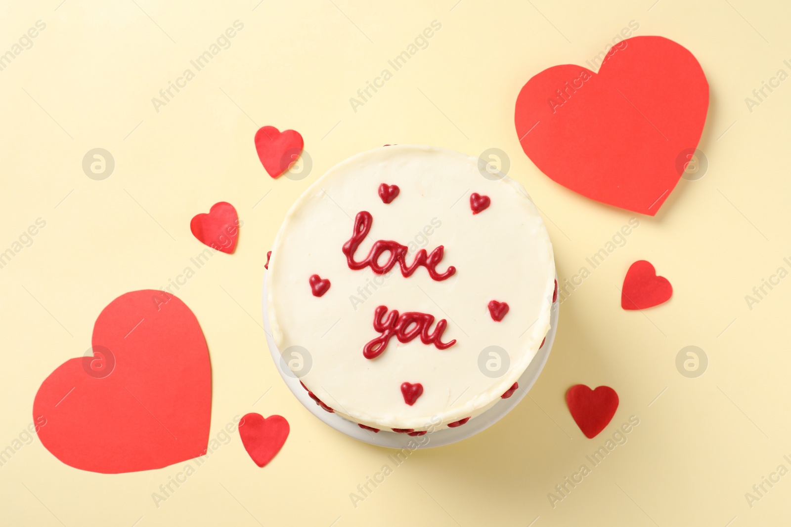 Photo of Bento cake with text Love You and paper hearts on beige table, top view. St. Valentine's day surprise