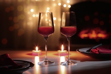 Photo of Glasses of wine and candles on table against blurred lights. Romantic dinner