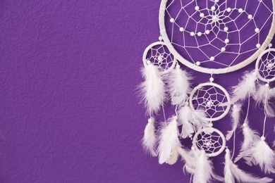 Photo of Beautiful handmade dream catcher on purple wall, closeup. Space for text