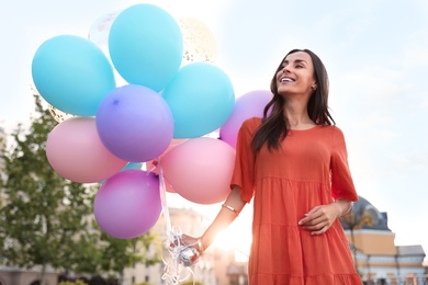 Photo of Cheerful young woman with color balloons outdoors on sunny day
