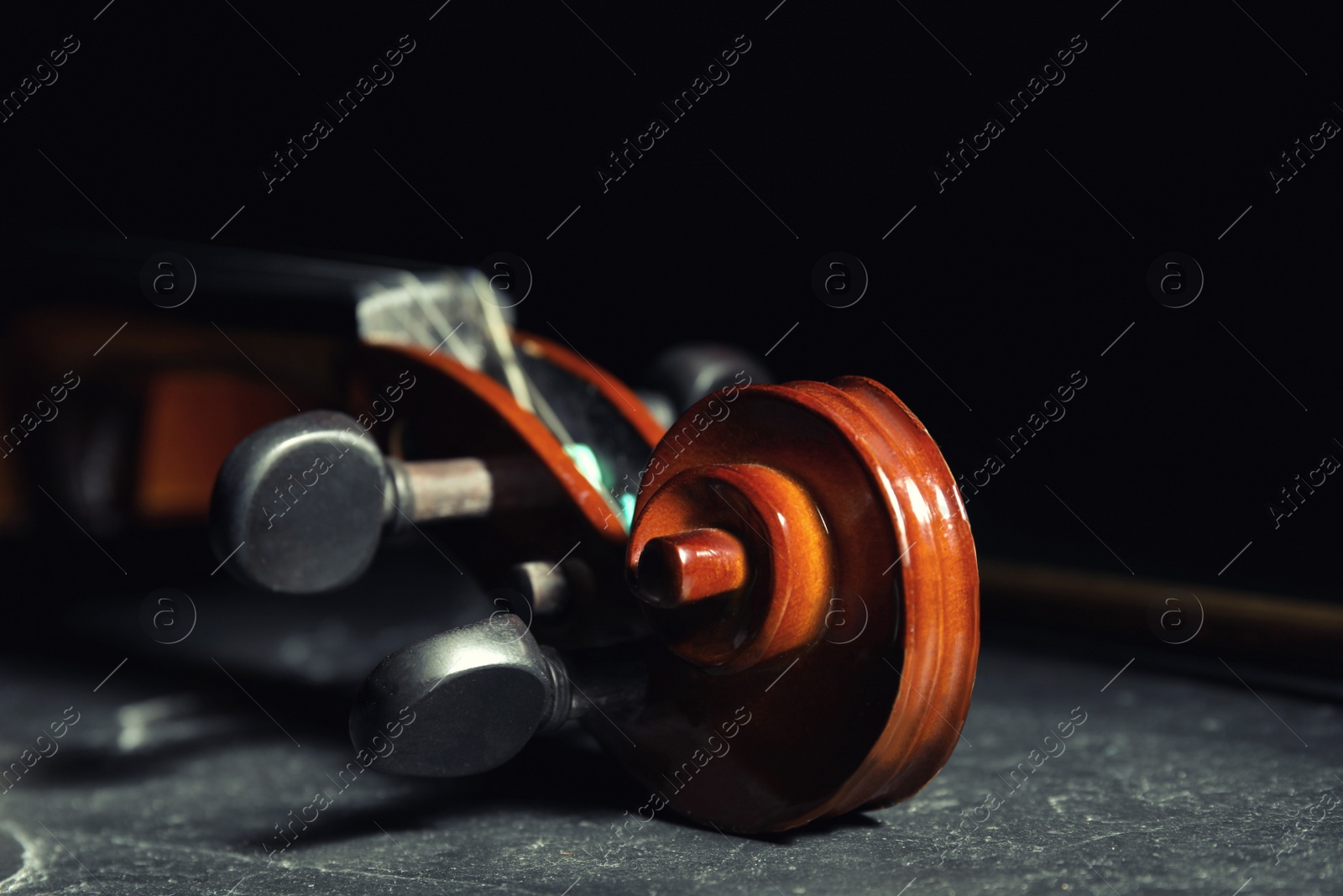 Photo of Classic violin on stone table against black background, closeup