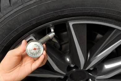 Photo of Man measuring car tire pressure with air gauge, closeup. Safety control