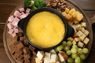 Photo of Fondue pot with melted cheese and different products on wooden table, top view