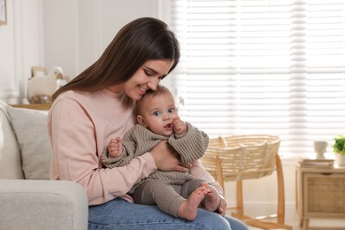 Photo of Happy young mother with her baby on sofa in living room. Space for text