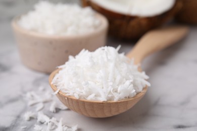 Photo of Coconut flakes in wooden spoon on white marble table, closeup