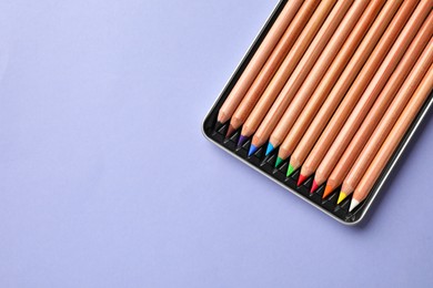 Photo of Box with many colorful pastel pencils on lilac background, top view and space for text. Drawing supplies