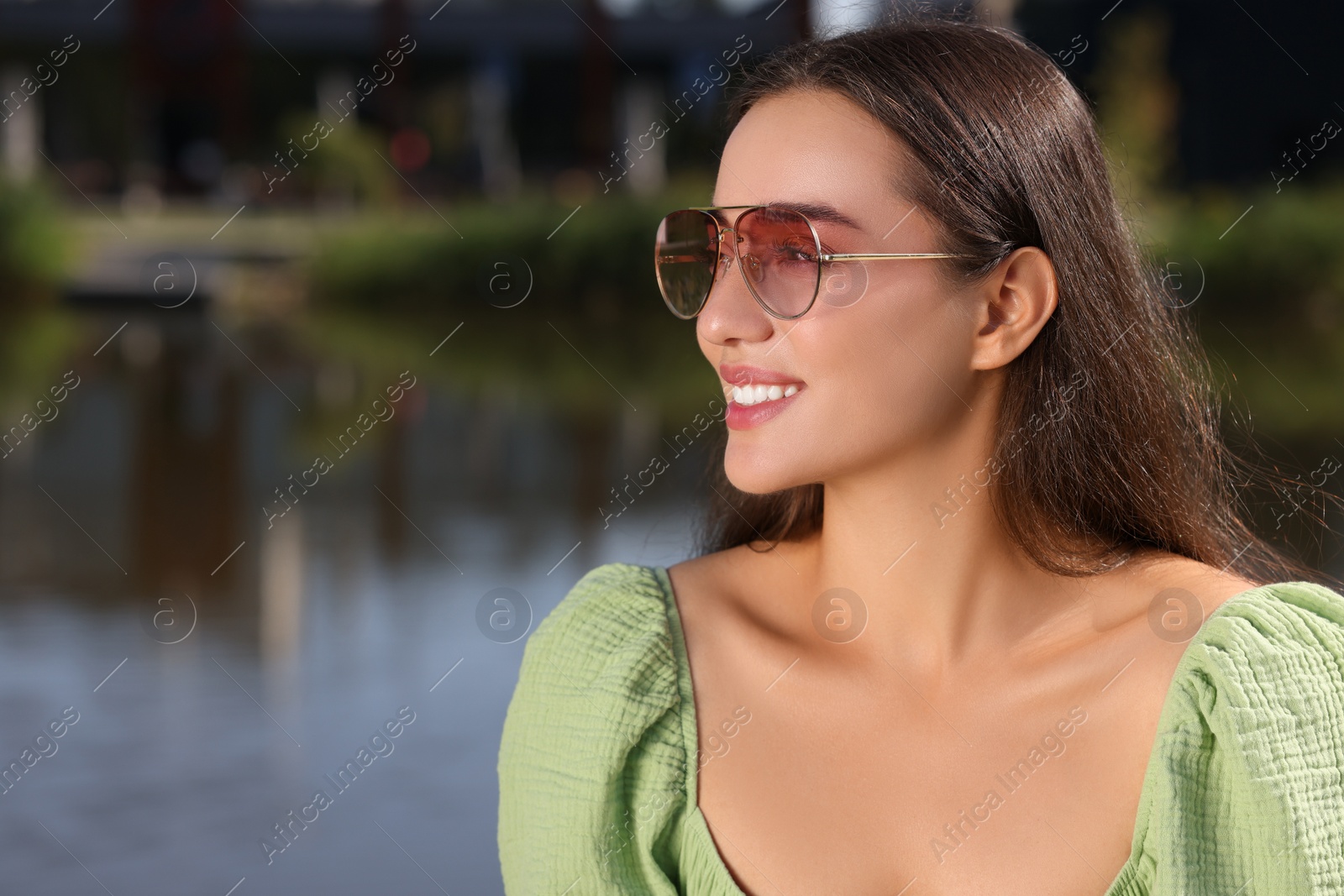 Photo of Beautiful smiling woman in sunglasses near river, space for text