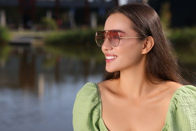 Beautiful smiling woman in sunglasses near river, space for text