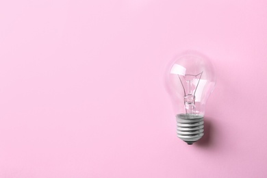 Photo of New incandescent lamp bulb on pink background, top view. Space for text