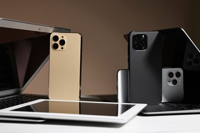 Photo of Many different modern gadgets on white table against brown background, closeup