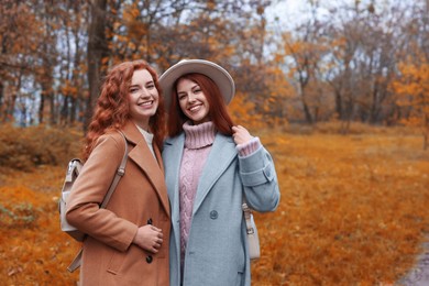 Photo of Portrait of beautiful young redhead sisters in park on autumn day. Space for text