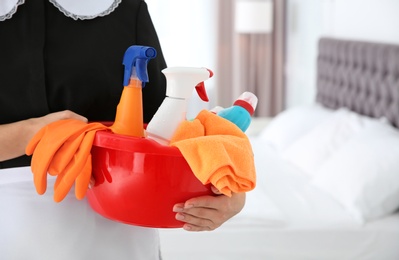 Photo of Young chambermaid with cleaning supplies in bedroom, closeup. Space for text