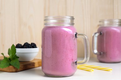 Photo of Mason jar of blackberry smoothie and mint on white wooden table