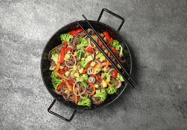 Photo of Stir fried noodles with mushrooms and vegetables in wok on grey table, top view