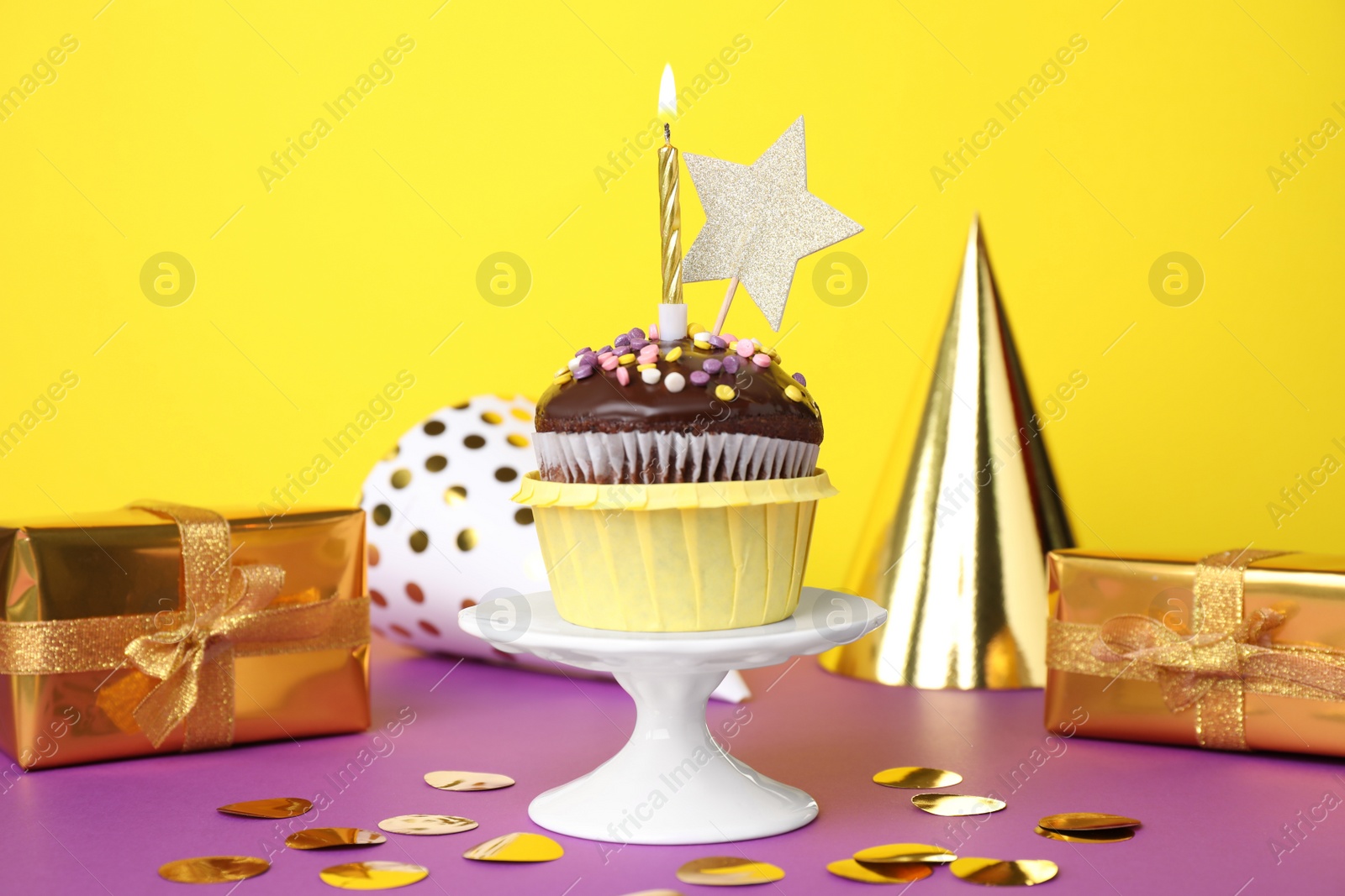 Photo of Delicious chocolate dessert with burning candle and party decor on purple table against yellow background