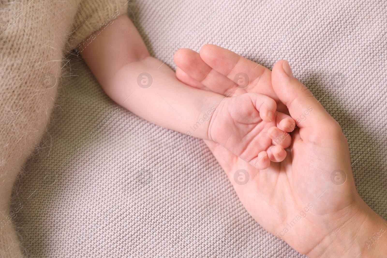 Photo of Mother and her newborn baby on light grey knitted plaid, top view