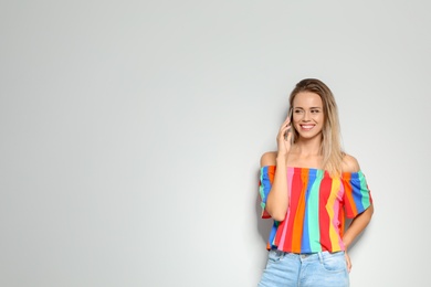 Beautiful woman talking on phone against light background