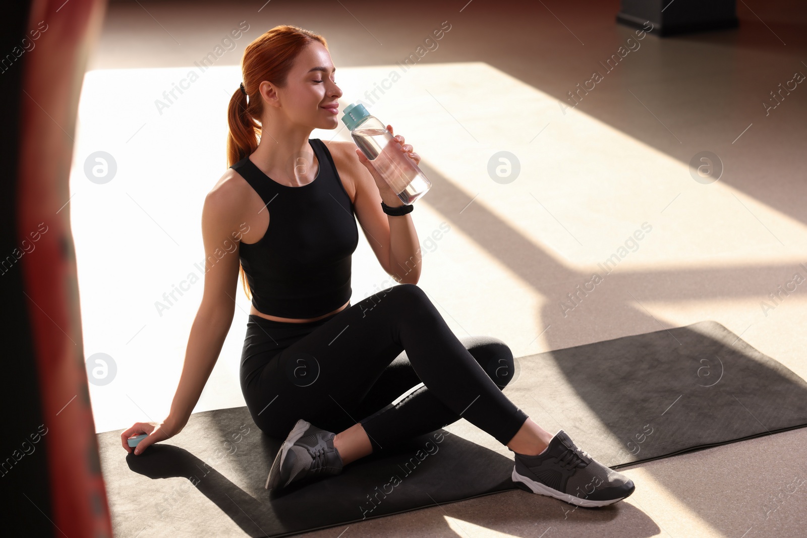 Photo of Athletic young woman with bottle of water on mat in gym, space for text