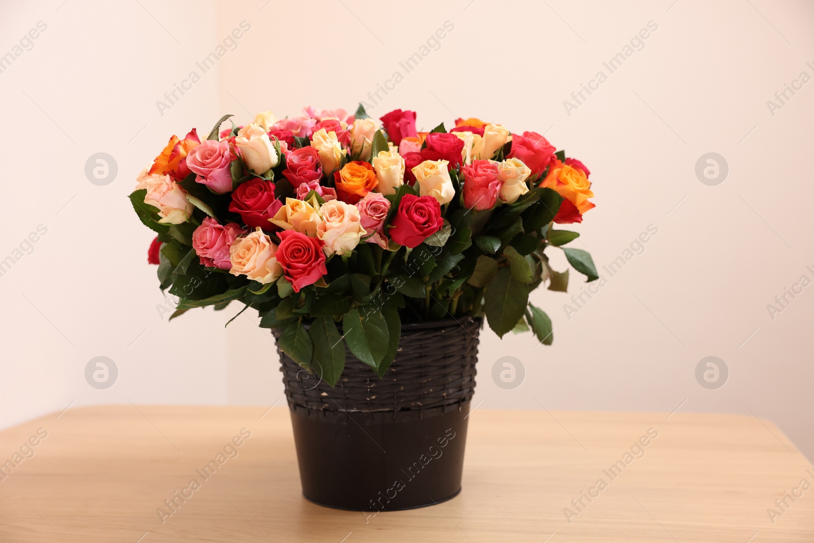 Photo of Bouquet of beautiful roses on wooden table against beige background