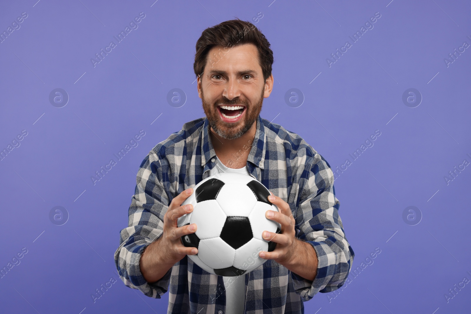 Photo of Emotional sports fan with soccer ball on purple background