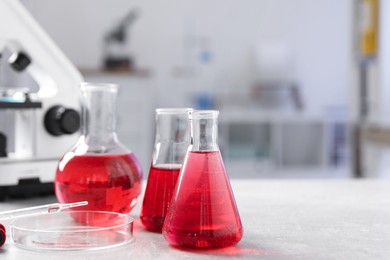 Photo of Laboratory analysis. Different flasks with red liquid and microscope on light grey table indoors