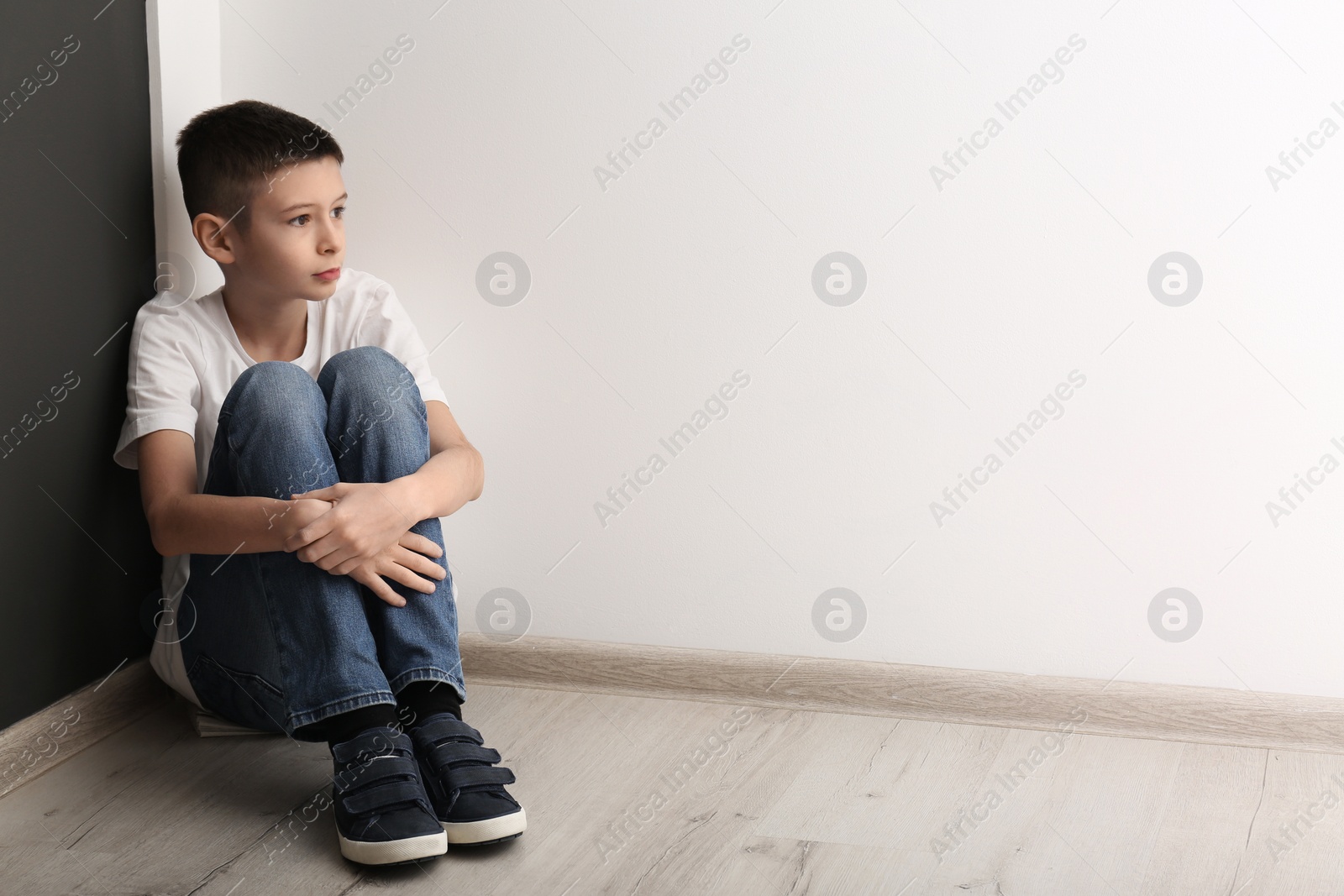 Photo of Upset boy sitting on floor indoors. Space for text