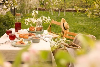 Photo of Stylish table setting with beautiful spring flowers, fruit drink and pie in garden