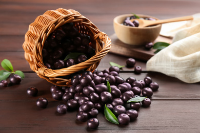 Photo of Basket and scattered acai berries on wooden table, closeup