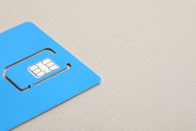 Light blue SIM card on beige background, closeup. space for text