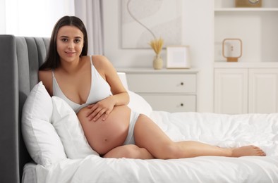 Beautiful pregnant woman in stylish comfortable underwear on bed at home