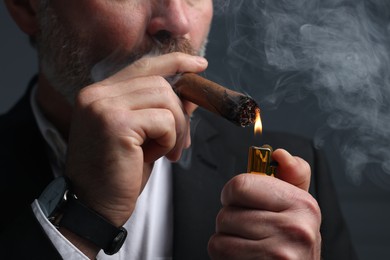 Bearded man lighting cigar on dark grey background, closeup