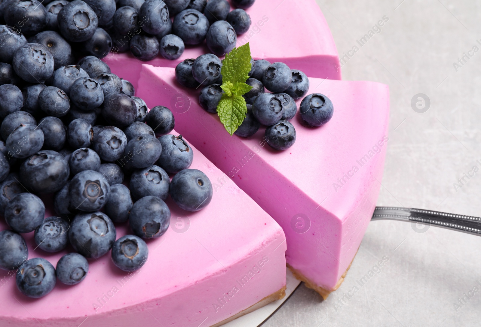 Photo of Cut tasty blueberry cake and shovel on light grey table, closeup