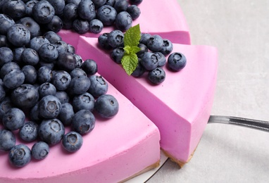 Photo of Cut tasty blueberry cake and shovel on light grey table, closeup