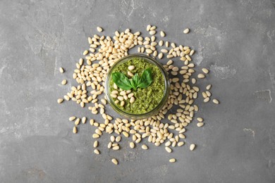 Photo of Jar with delicious pesto sauce, pine nuts and basil leaves on grey table, flat lay