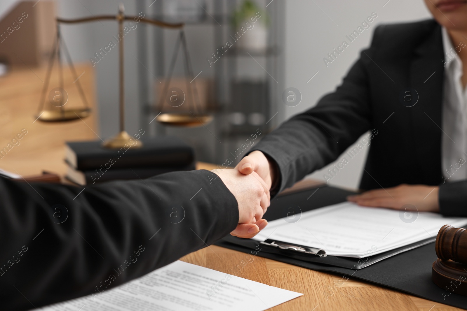 Photo of Notary shaking hands with client at wooden table in office, closeup