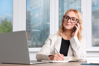 Lady boss talking on smartphone near laptop in office. Successful businesswoman