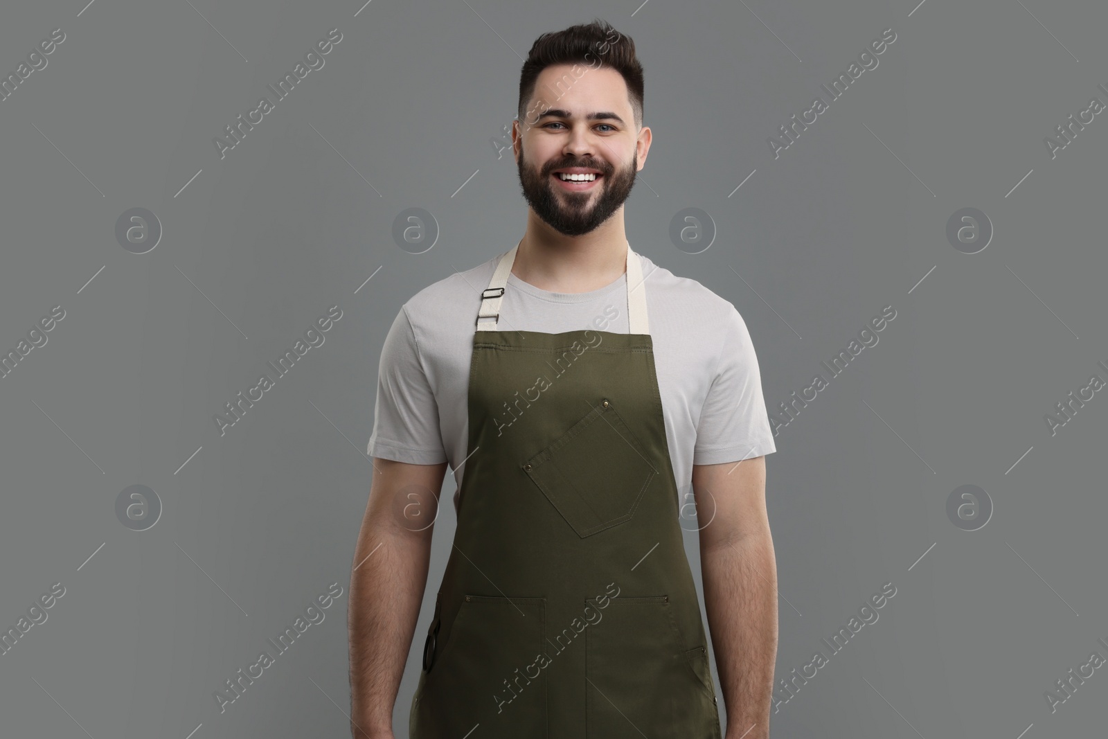 Photo of Smiling man in kitchen apron on grey background. Mockup for design